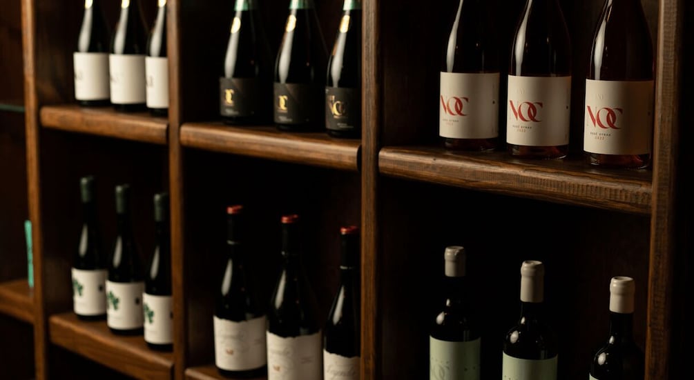 A collection of wine bottles on wooden shelves. 2