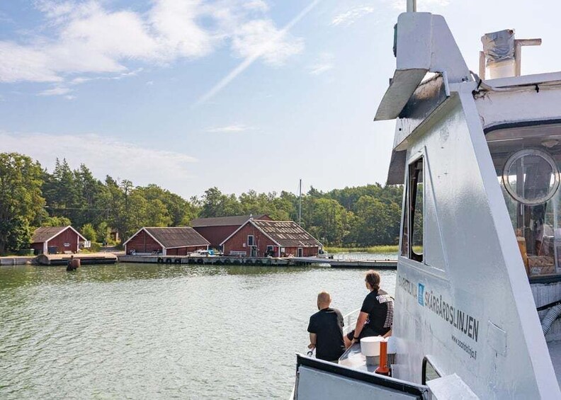 A boat with two people on deck, a dock with red buildings, and a calm river. 2