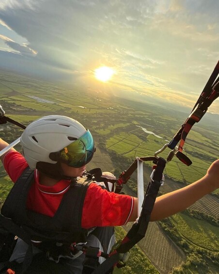 A person in a red shirt and helmet, holding onto a paraglider's control bar. 3