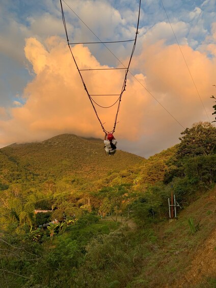 A person suspended by a harness, swinging on a cable, with a mountainous landscape and a cloudy sky in the background. 1