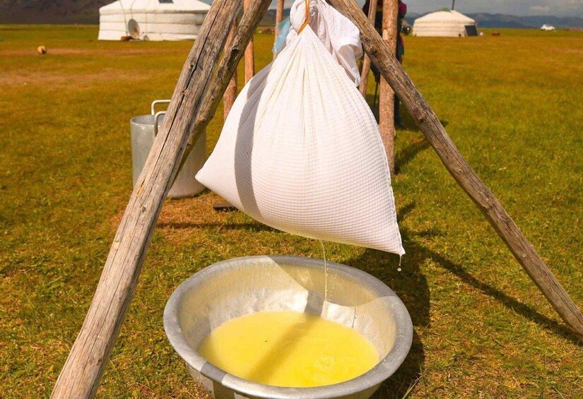 A traditional yurt with a white bag hanging from a wooden frame, a metal bowl on the ground, and a grassy field in the background. 3