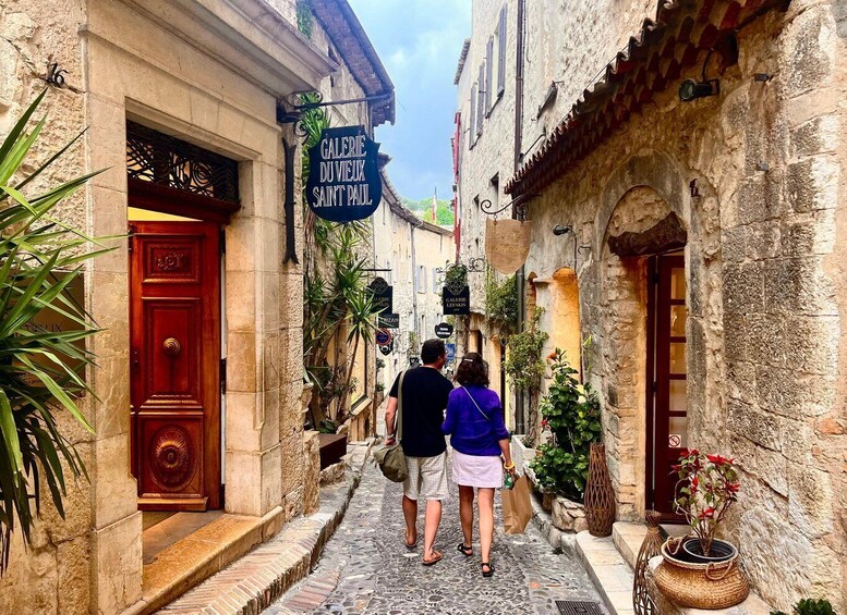 A narrow cobblestone street with buildings, a red door, and hanging signs for 'Galerie du Vieux Saint Paul'. 5