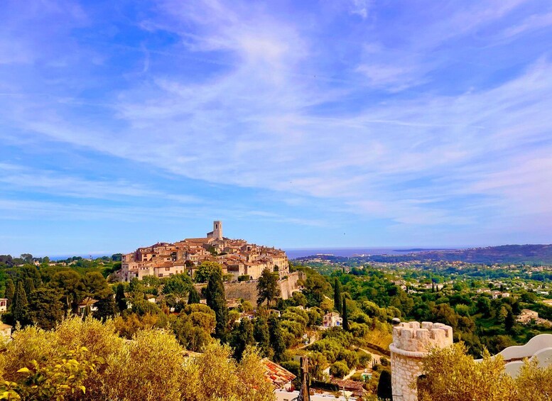 A historic hilltop town with a prominent tower, surrounded by lush greenery and a clear blue sky. 1
