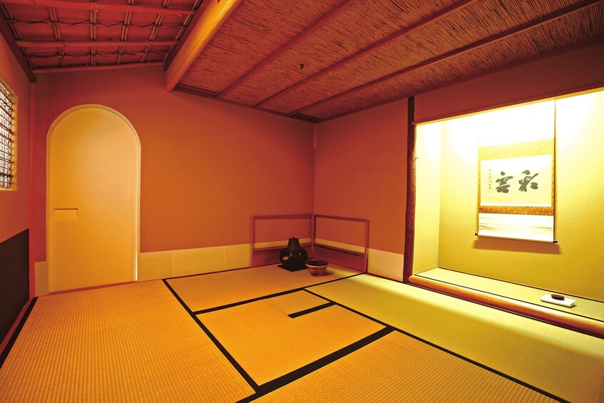 A tatami mat room with a wooden ceiling, a sliding door, and a wall-mounted picture frame. 2
