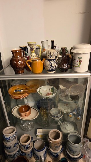A variety of ceramic items on shelves and in a display case, including pitchers, mugs, and plates with floral and geometric patterns. 5