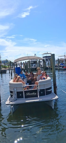 A group of people on a boat with a 'Bentley' sign, docked at a pier with other boats and a clear sky. 4