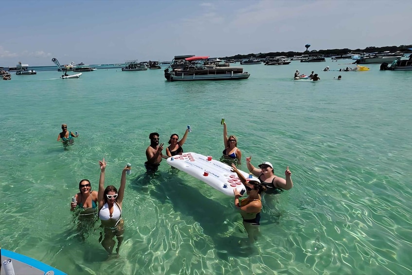 A group of people in clear turquoise water, holding a white inflatable board. 3