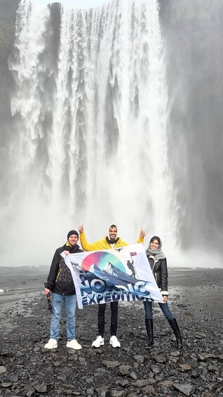 A group of people standing in front of a waterfall with a banner. 1