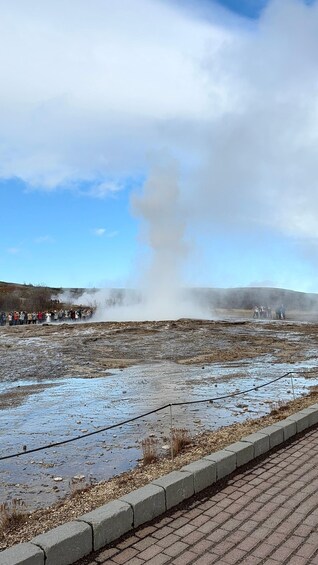 A geothermal area with steam rising, a crowd of people observing, and a clear sky. 5