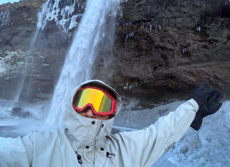 A person in a white jacket and goggles standing in front of a waterfall with ice formations. 3
