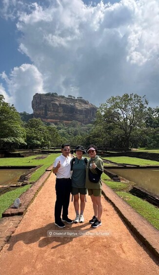 Three people standing on a pathway with a large rock formation in the background. 4