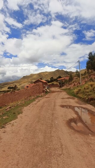 A rural dirt road with houses, a mountain in the background, and a cloudy sky. 3