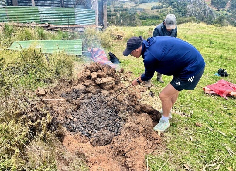 Two people digging a hole in a grassy area with a pile of rocks and a green corrugated metal sheet in the background. 4