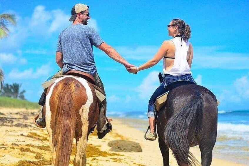 Two people riding horses on a beach with the ocean in the background. 1