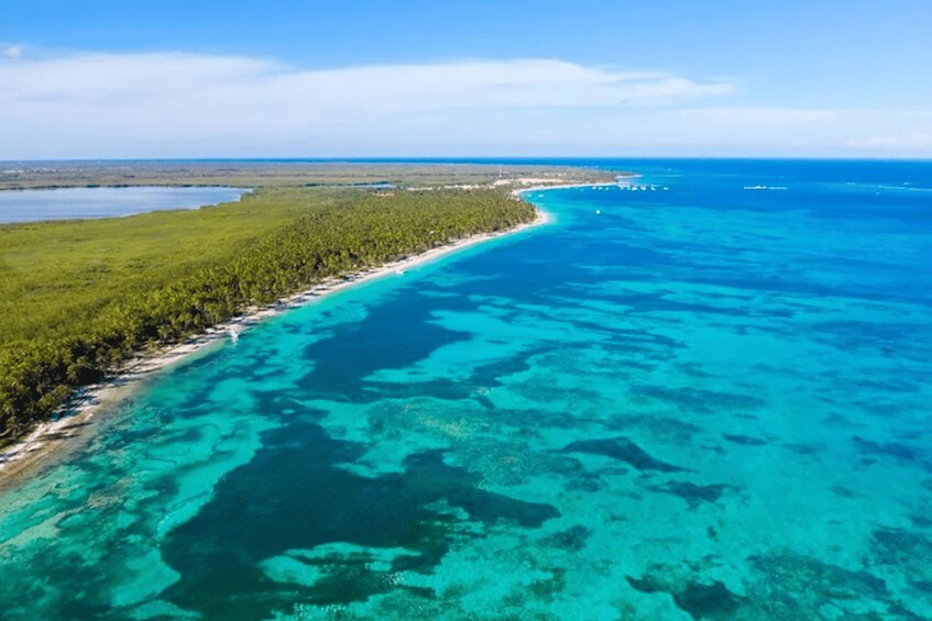 A coastal landscape with a clear turquoise sea, a sandy beach, and a dense forested area. 5