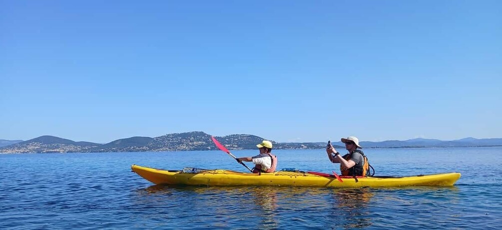 Two people kayaking on a calm body of water with a clear sky and distant hills. 2