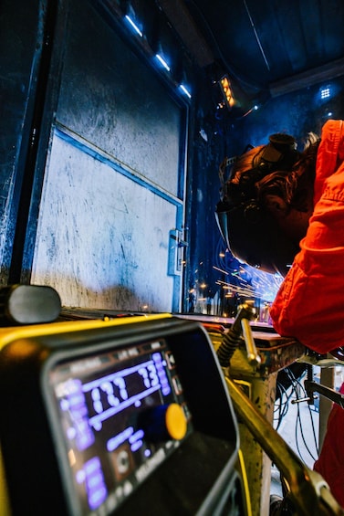 A person welding on a metal structure with sparks, wearing protective gear and a red jacket. 5
