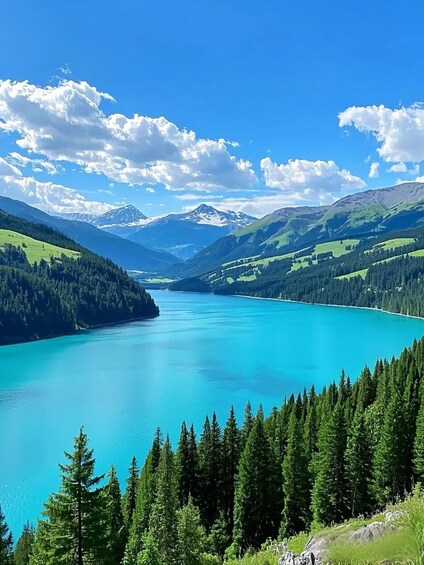 A turquoise lake surrounded by green hills and mountains under a clear blue sky. 2