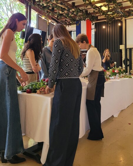 A group of people at a table with a white tablecloth, surrounded by greenery and flowers. 2
