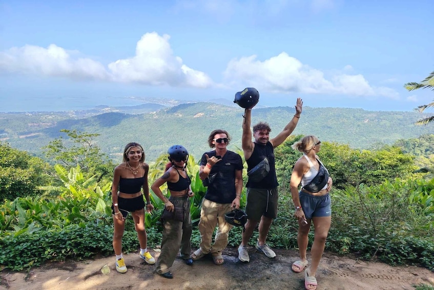 A group of people standing on a hill with a scenic view of a valley and mountains in the background. 1