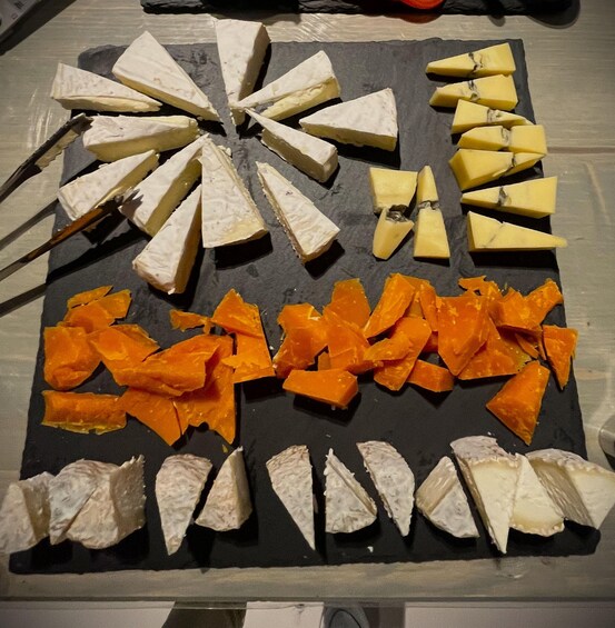 A variety of cheeses and fruits arranged on a black slate board. 4