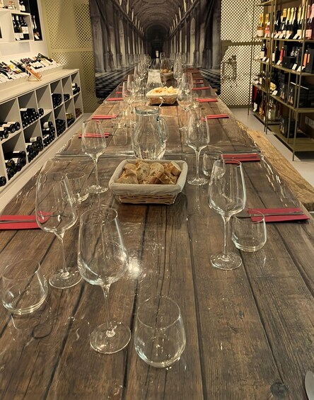 A long table with empty wine glasses and a basket of bread in the center, surrounded by shelves of wine bottles. 5