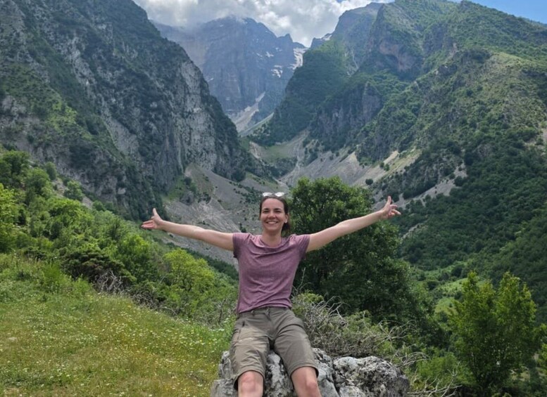 A person sitting on a rock with arms outstretched, surrounded by a mountainous landscape. 5
