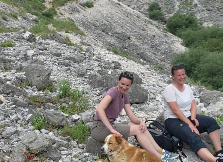 Two people sitting on a rocky hillside with a dog. 2
