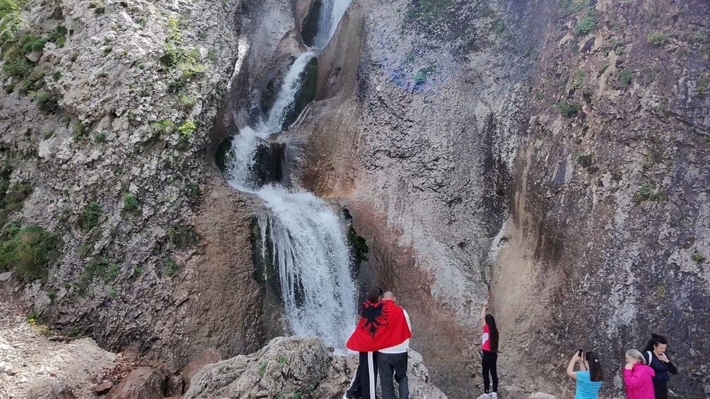 A waterfall cascading down a rocky cliff with a group of people observing it. 4