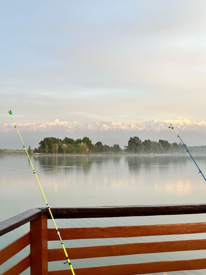 A calm lake with fishing rods, a wooden dock, and snow-capped mountains in the distance. 1