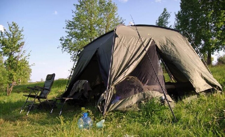 A tent set up in a grassy field with trees in the background. 2