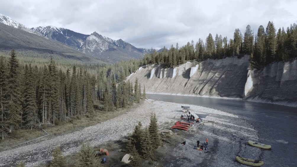 A river with a rocky shore, surrounded by dense forest and mountains in the background. 4