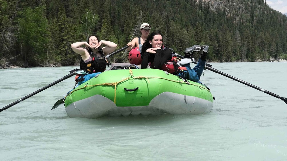 A group of people on a green inflatable raft on a river surrounded by forest. 5