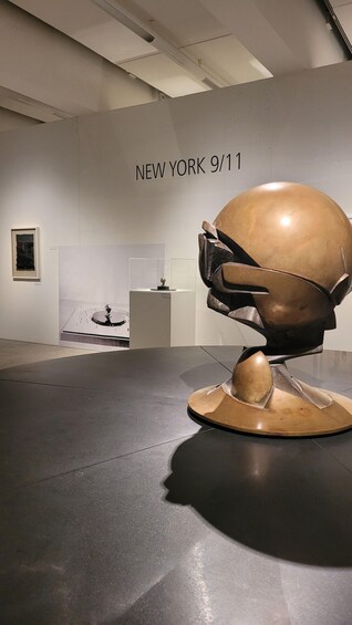 A sculpture of a helmet on a pedestal in an art gallery with a wall sign reading 'NEW YORK 9/11'. 4