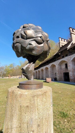 A sculpture of a brain on a pedestal in a park with a brick building in the background. 3