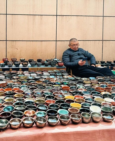 A man sitting among an array of bowls and pots. 3