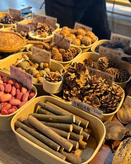 A variety of dried plants and nuts displayed in containers at a market. 1