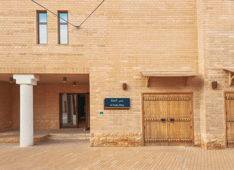 A building with a sign reading 'Al Hula Al Bayah' in Arabic, a wooden gate, and a brick facade. 3