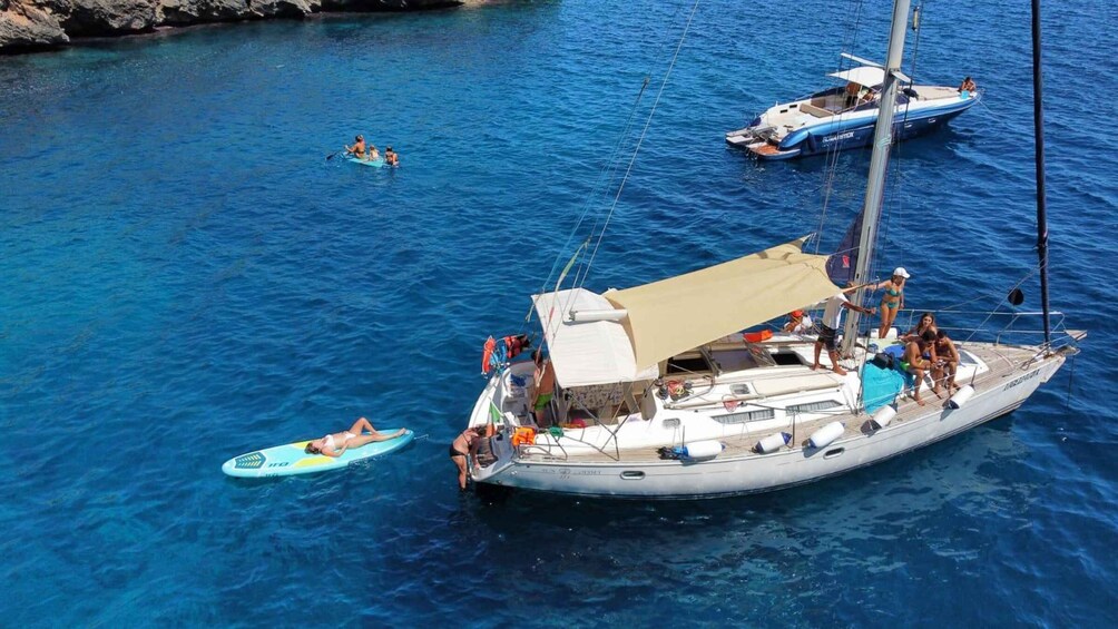 A sailboat with people on deck and a person on a stand-up paddleboard in the water. 1