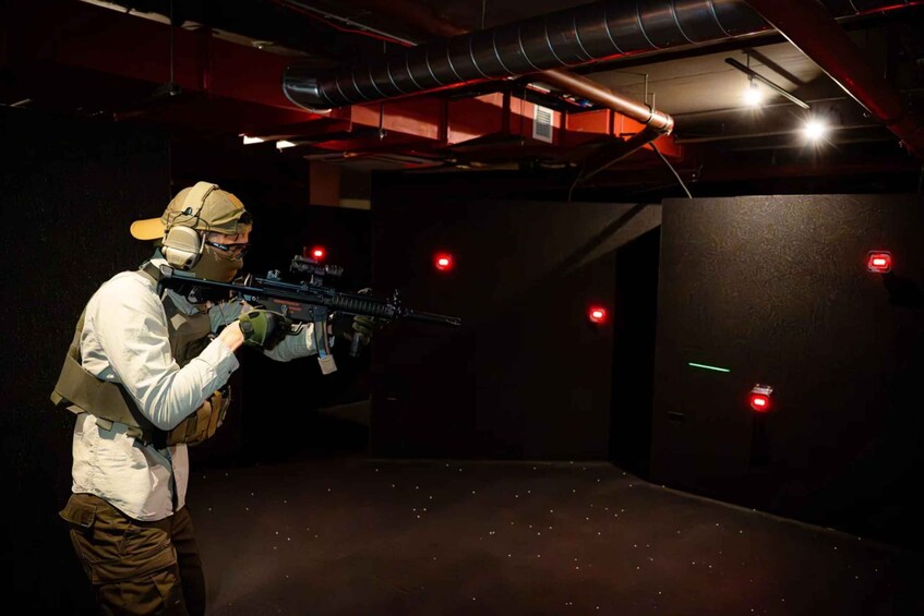 A person aiming a rifle in a shooting range with targets and red lights. 2