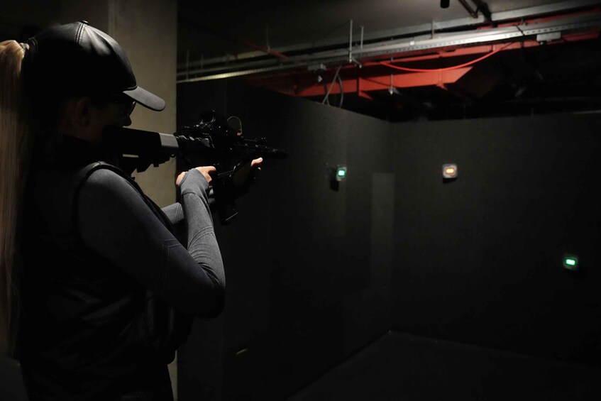 A person aiming a rifle in a dimly lit indoor shooting range. 1