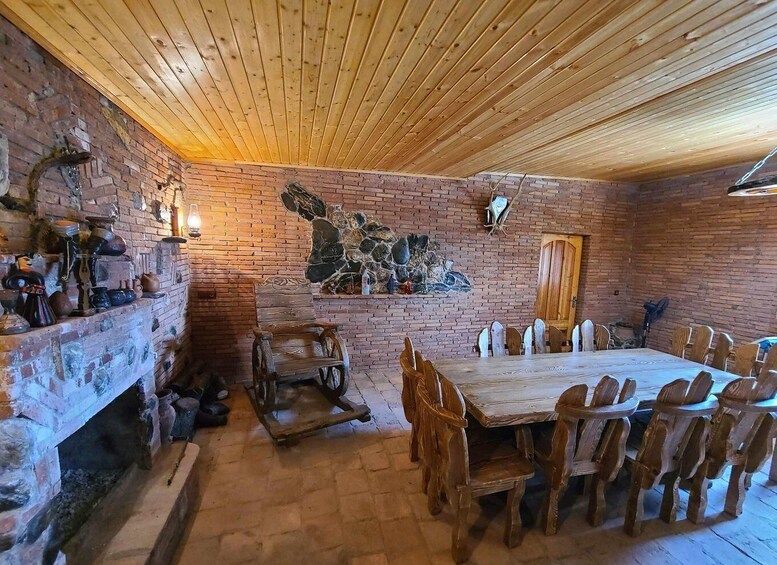 A rustic dining area with a long wooden table and chairs, a brick fireplace, and a wooden ceiling. 2