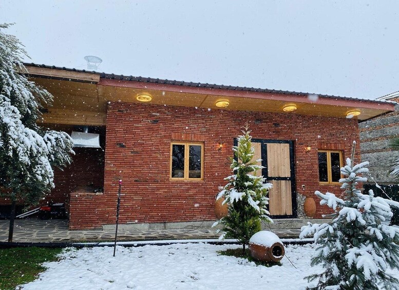 A brick house with a snow-covered lawn and a small evergreen tree in the foreground. 1