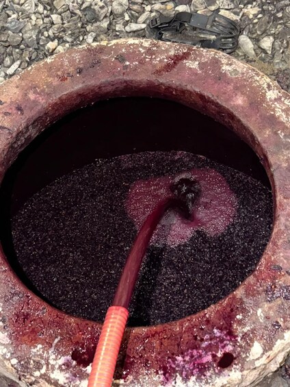 A rusty metal container with a spout, filled with a dark liquid, possibly wine or juice, and a small amount of sediment at the bottom. 2