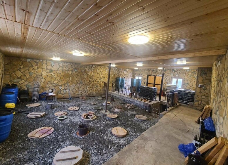 A rustic interior with stone walls, wooden beams, and a gravel floor. 4