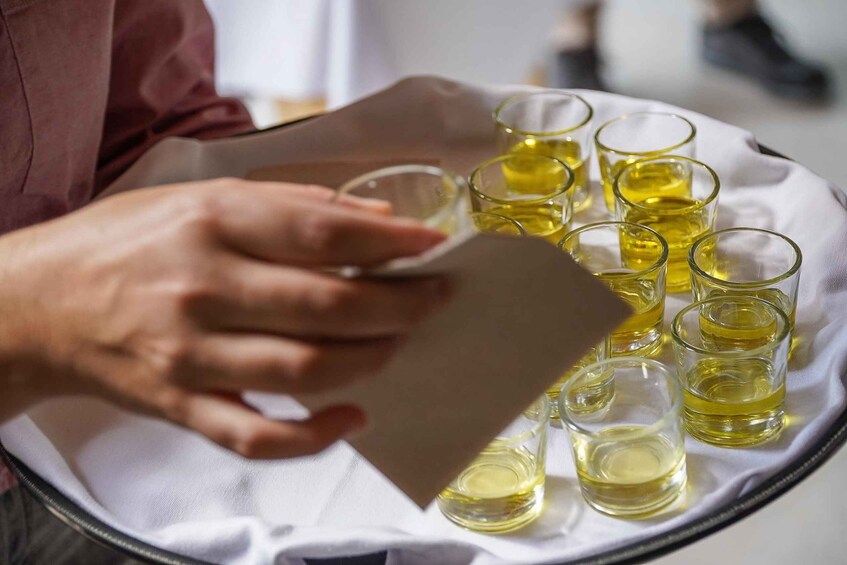 A person pouring a liquid from a bottle into shot glasses on a tray. 1