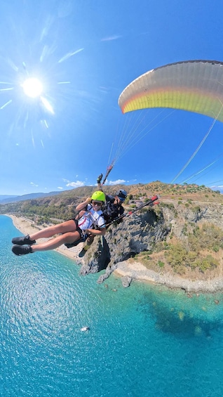 A person paragliding over a coastal cliff with a clear blue sea below. 1