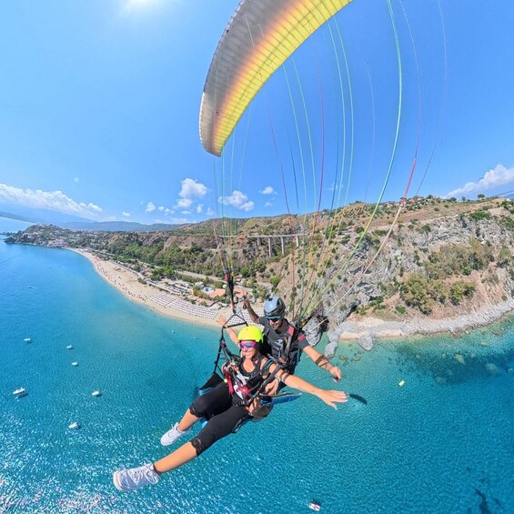 A person paragliding over a coastal area with clear blue waters and a beach in the background. 4