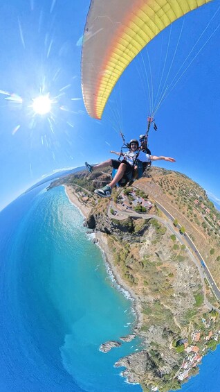 A person paragliding over a coastal landscape with a clear sky and a bright sun. 5