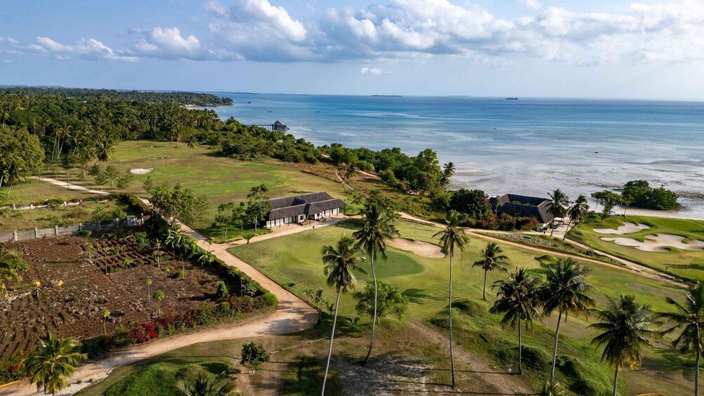 A golf course with a clubhouse, palm trees, and a view of the ocean. 4